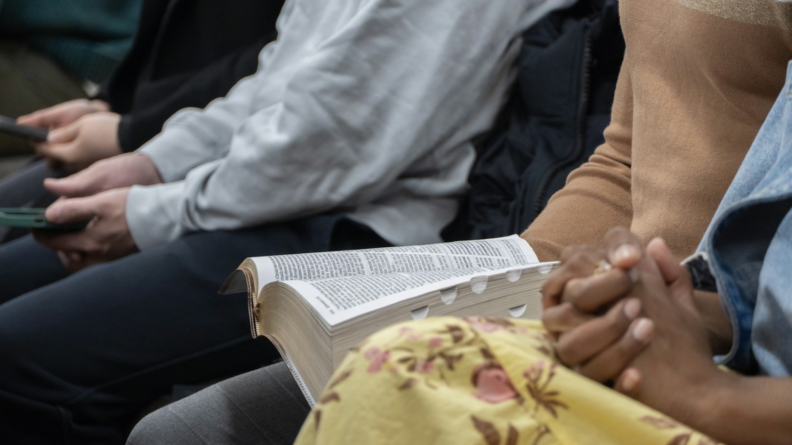An open Bible resting on a worshipper’s lap, with people seated alongside